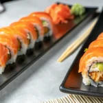 Close-up of fresh salmon sushi rolls served on black plates with chopsticks, soy sauce, wasabi, and pickled ginger on the side.