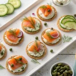 Smoked salmon mini bites elegantly arranged on a serving platter with fresh herbs and a creamy topping.