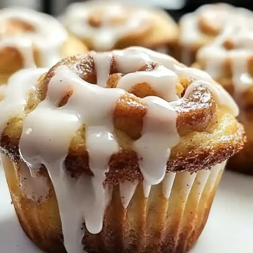 Close-up of cinnamon roll muffins topped with icing on a white plate
