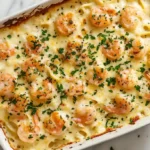 A creamy shrimp scampi pasta bake topped with golden shrimp and fresh parsley in a white ceramic baking dish.