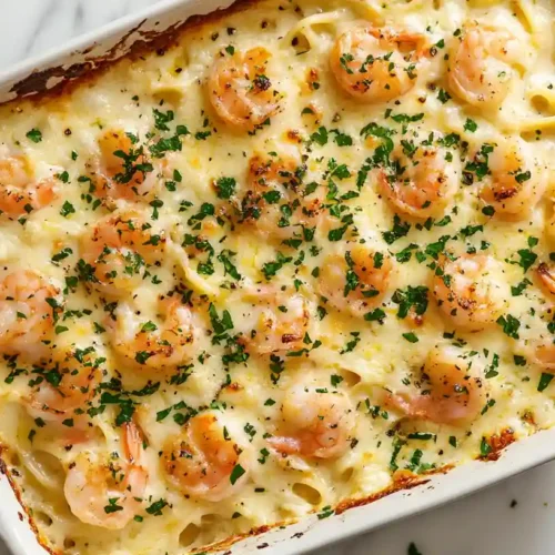 A creamy shrimp scampi pasta bake topped with golden shrimp and fresh parsley in a white ceramic baking dish.