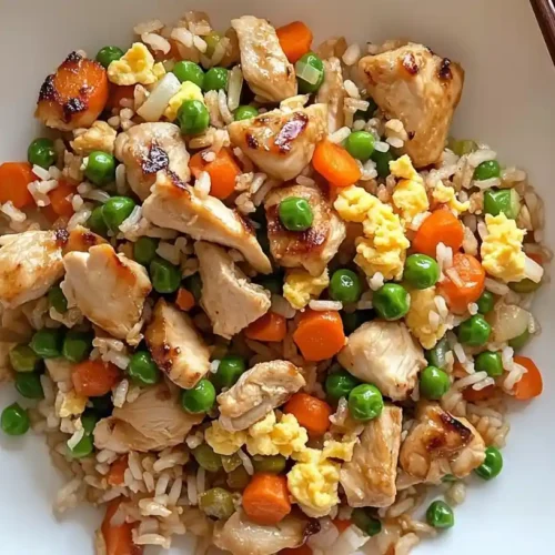 Top-down view of chicken fried rice with vegetables and scrambled egg in a white bowl with chopsticks.