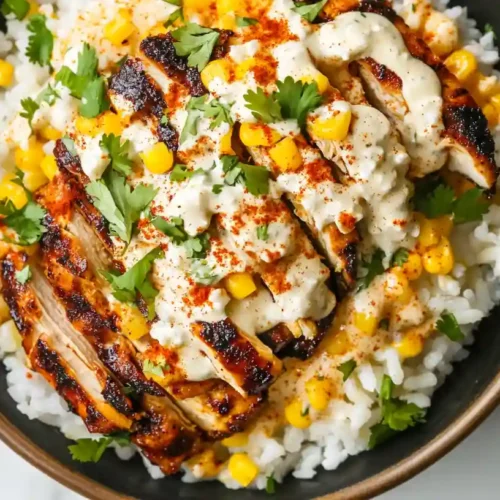 A top-down view of a street corn chicken rice bowl with grilled chicken, white rice, corn, creamy sauce, cilantro, and spices.