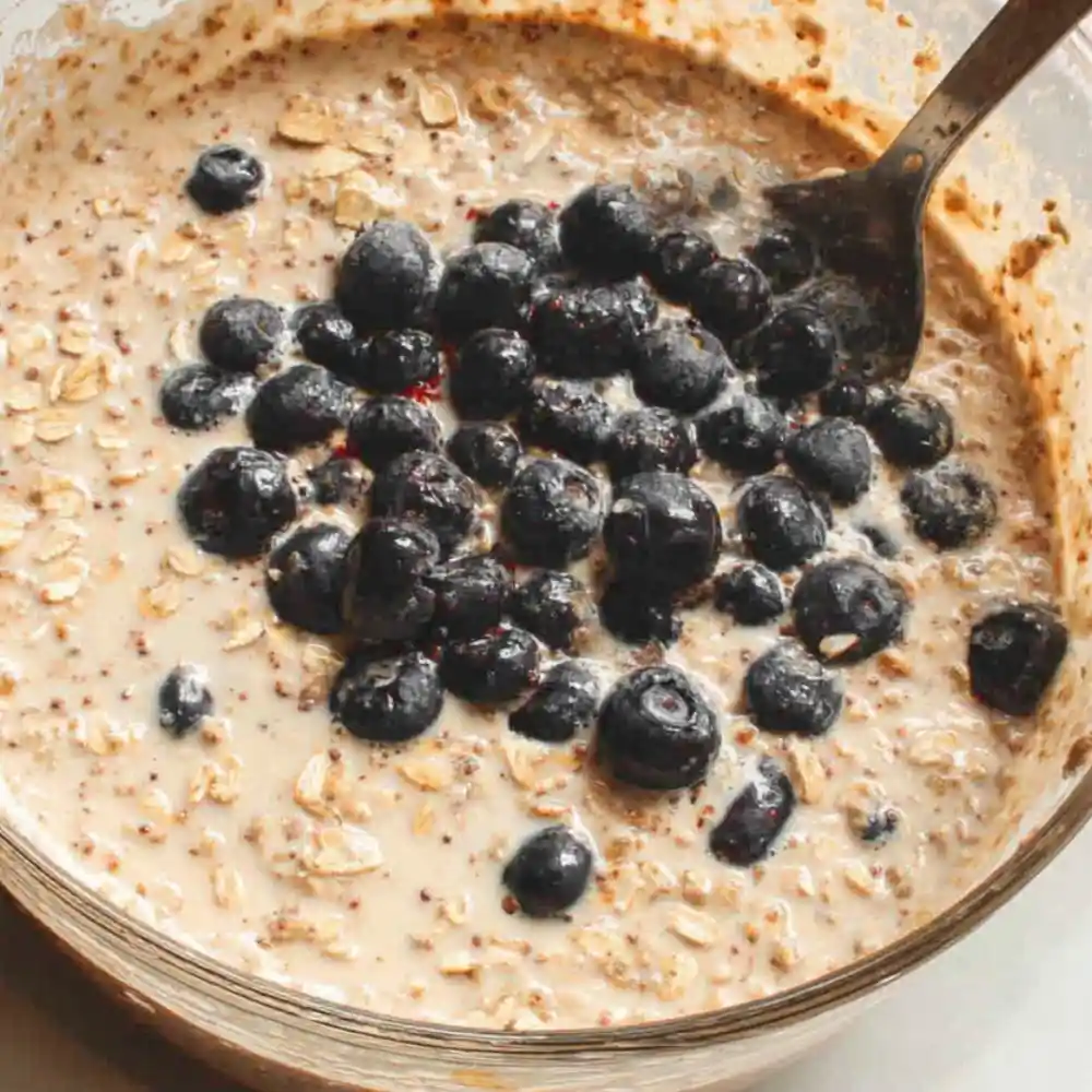 Blueberries, oats, and wet ingredients mixed in a bowl for baked oatmeal preparation.