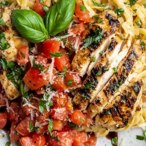 Top-down view of Bruschetta Chicken Pasta with grilled chicken, fresh tomato bruschetta, pasta, and basil garnish.