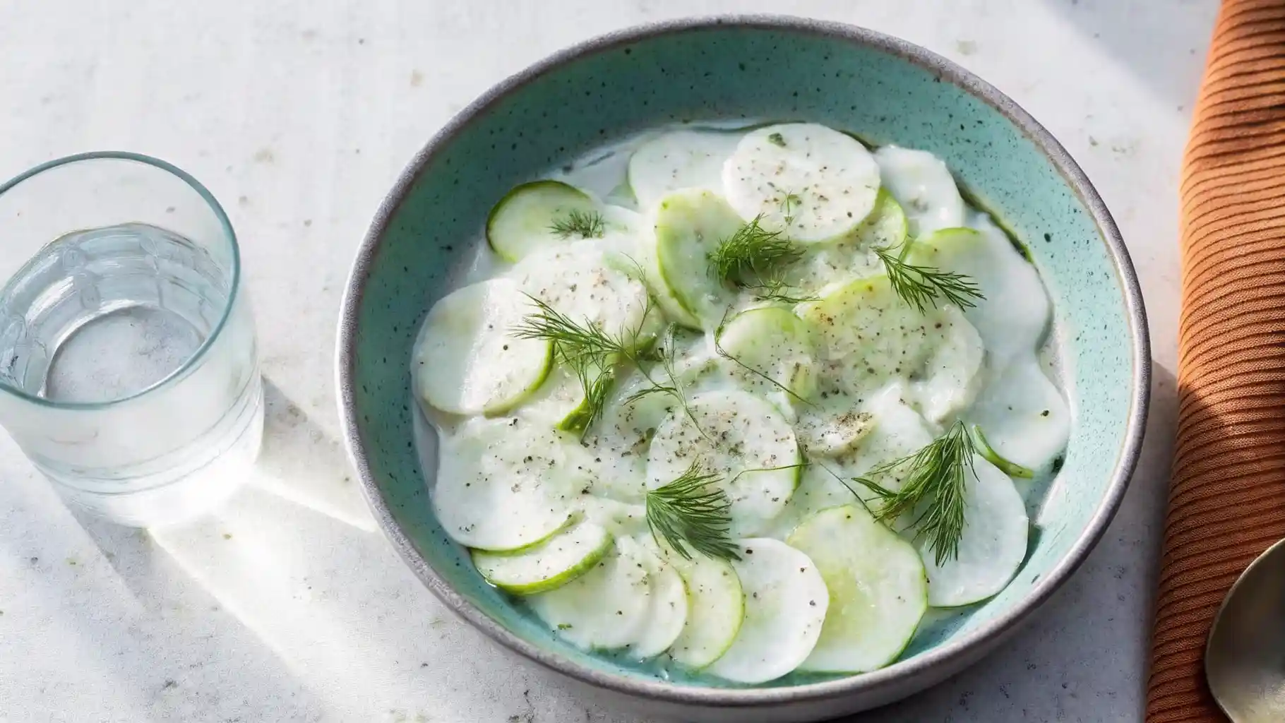 Bowl of creamy cucumber salad garnished with fresh dill and black pepper.