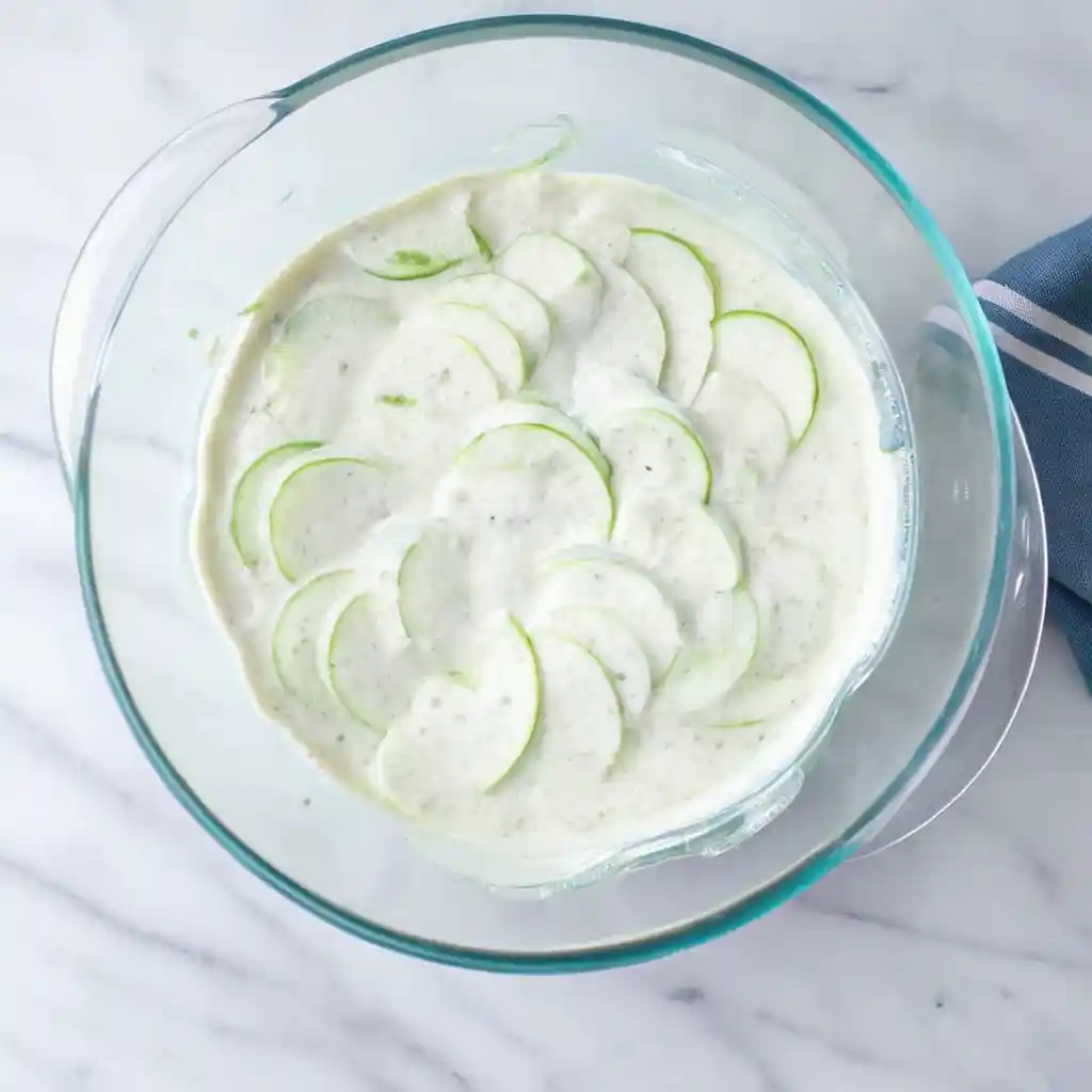 Thinly sliced cucumbers layered in creamy dressing in a clear glass bowl.