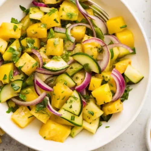 Pineapple cucumber salad with red onion and herbs served in a white bowl on a light surface.