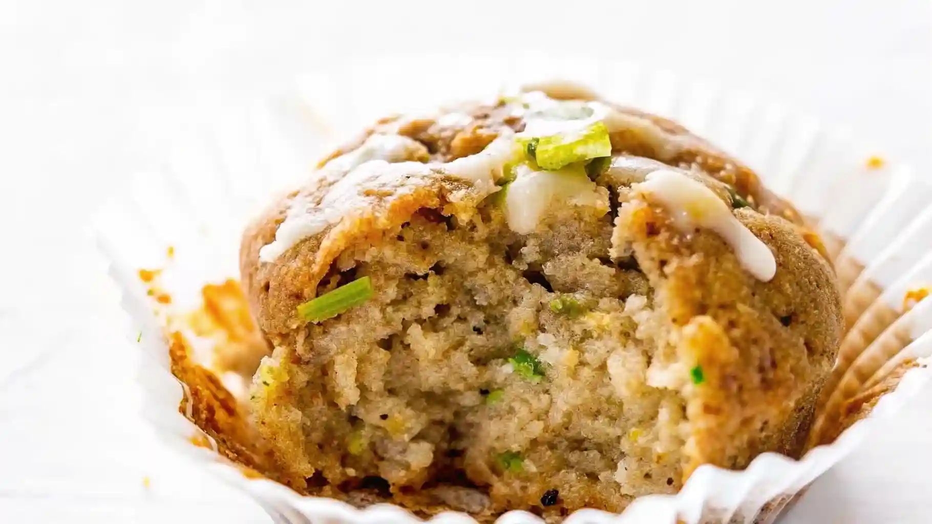 Close-up of a moist banana zucchini muffin with a bite taken, showing soft texture and flecks of green zucchini.
