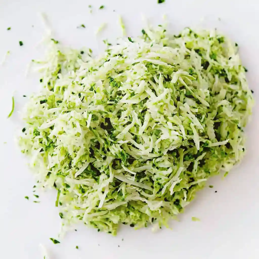 Freshly grated zucchini on a white surface, ready for baking banana zucchini muffins.