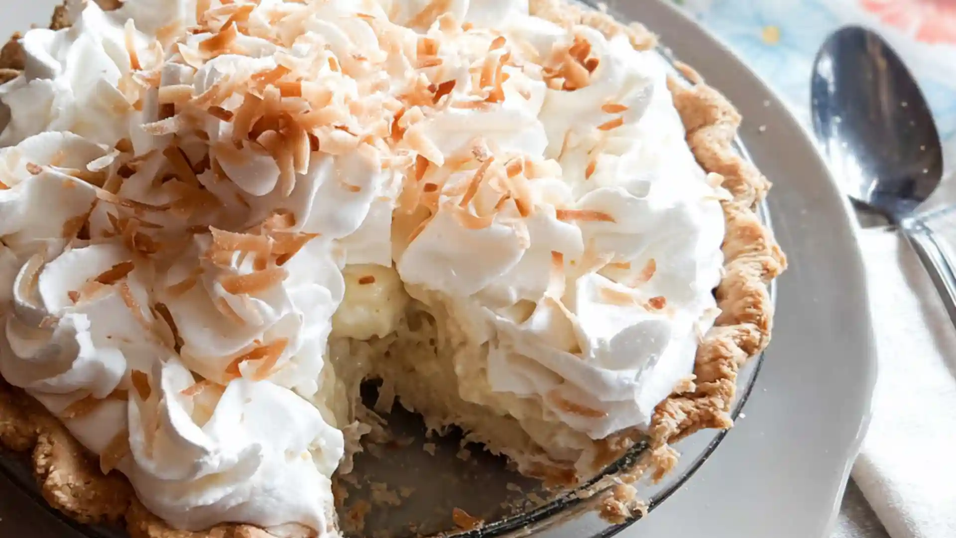 Coconut cream pie with whipped cream swirls and toasted coconut flakes in a flaky crust, served on a plate.