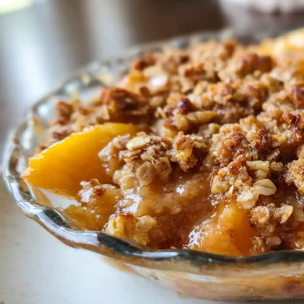 Close-up of baked peach crisp with golden oat topping in a glass dish.