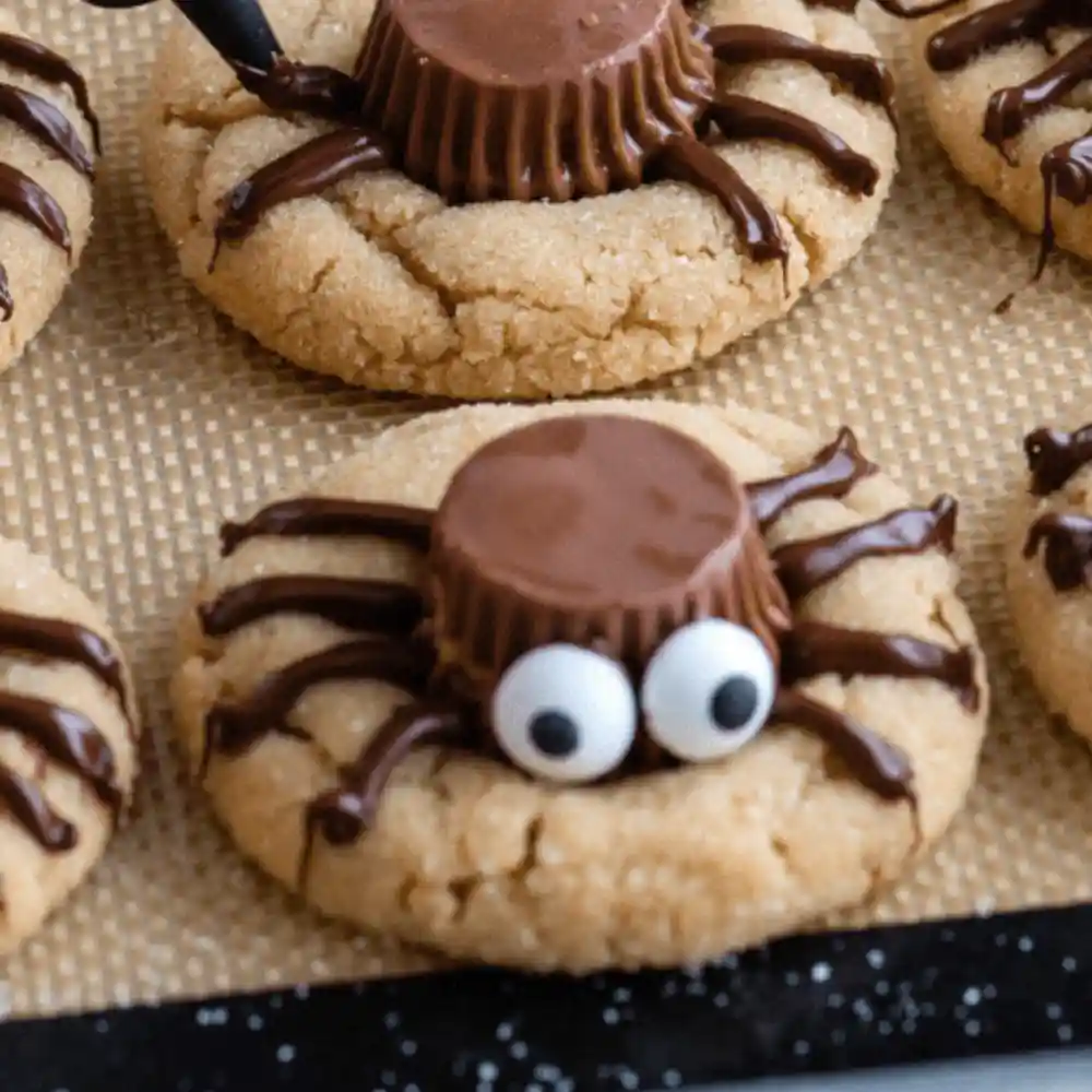 Peanut Butter Spider Cookies with Reese’s cups, candy eyes, and piped chocolate legs on a silicone baking mat.