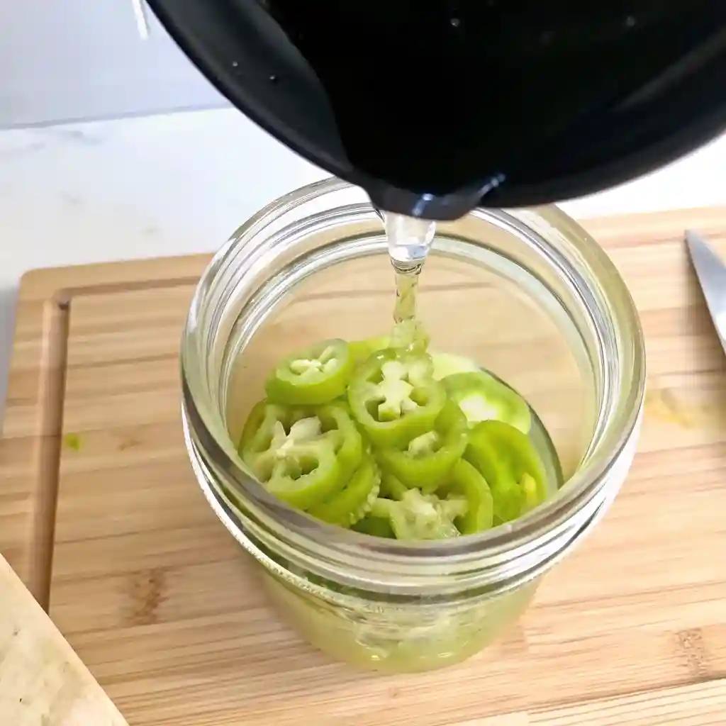 Hot brine being poured over sliced banana peppers in a mason jar