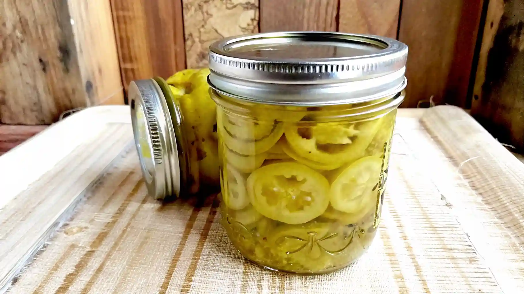 Jar of pickled banana pepper rings on a wooden board