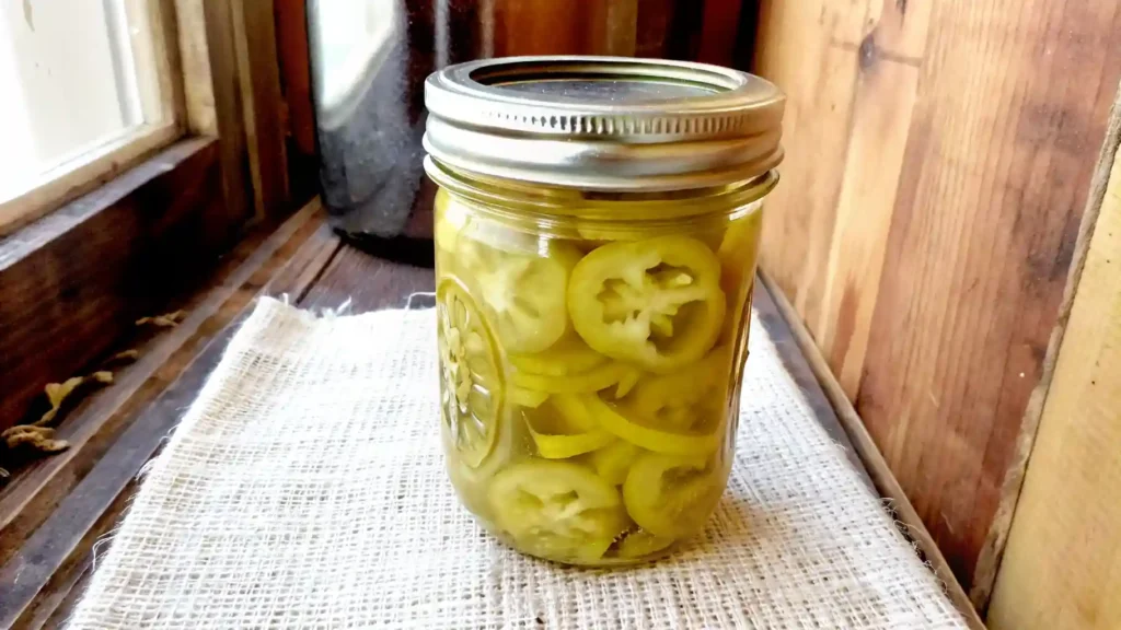 Jar of homemade pickled banana pepper rings on a rustic windowsill