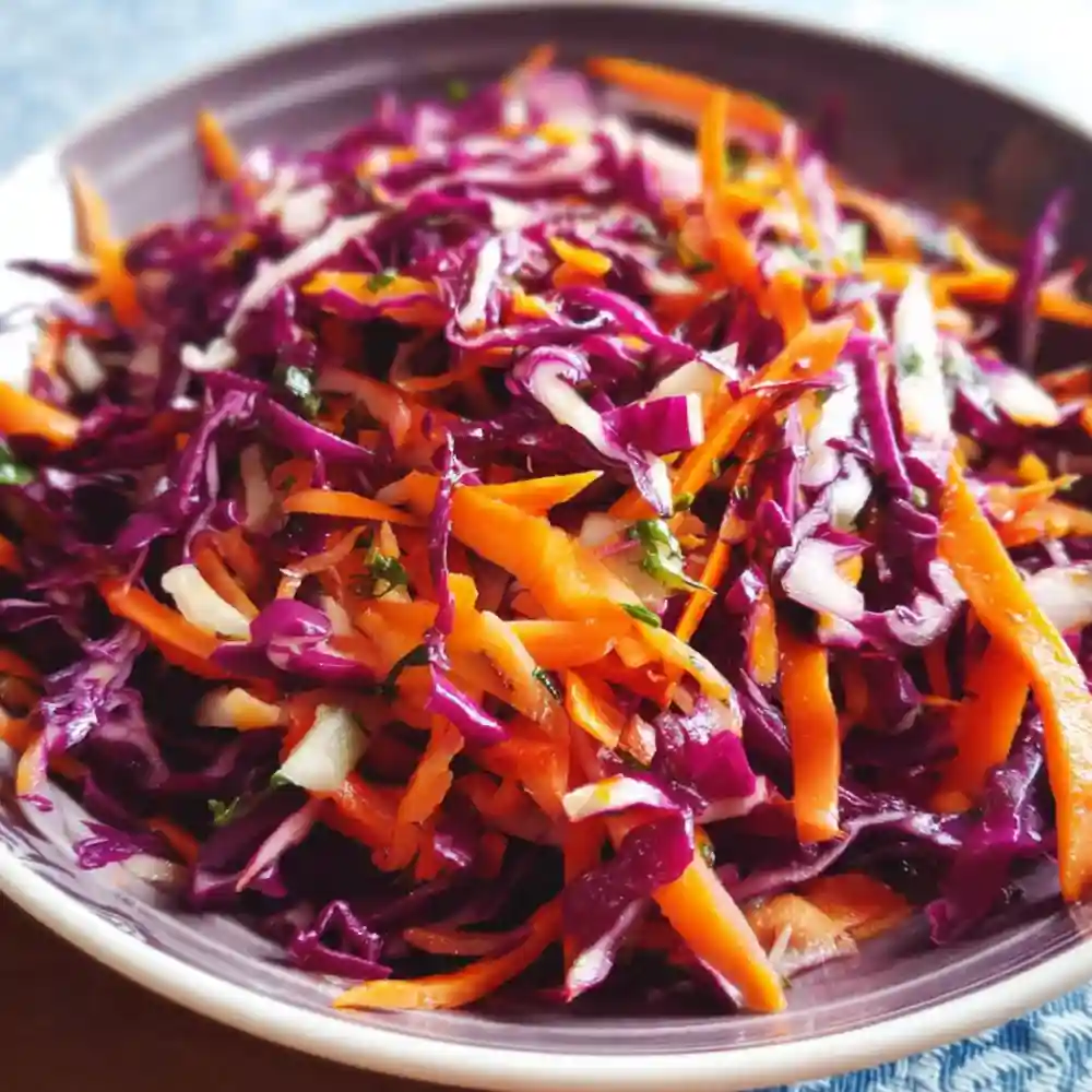 Bright red cabbage and carrot slaw in a shallow dish with fresh herbs