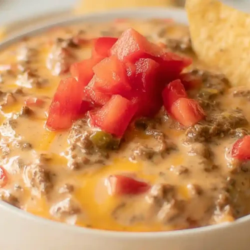 Bowl of creamy Rotel dip with ground beef, topped with diced tomatoes and served with tortilla chips.