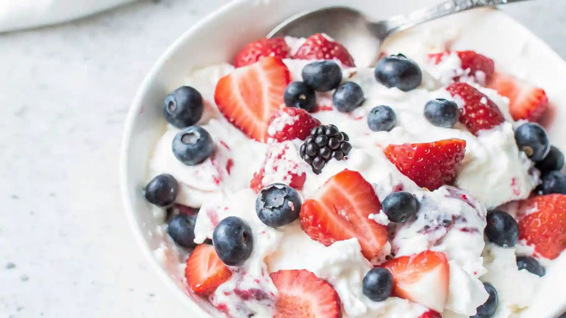 Close-up of triple berry cheesecake fruit salad with strawberries, raspberries, blackberries, and blueberries in creamy filling.