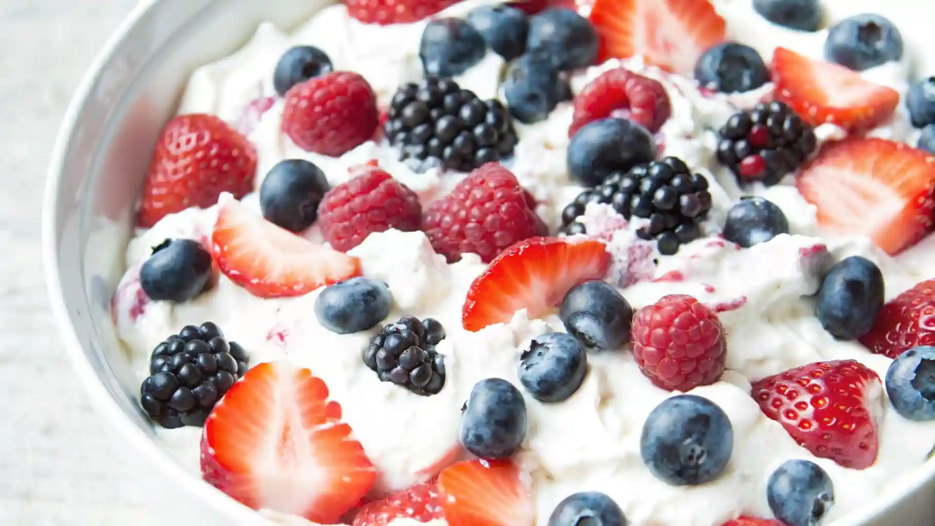 Bowl of triple berry cheesecake fruit salad with strawberries, blueberries, and blackberries in creamy filling.