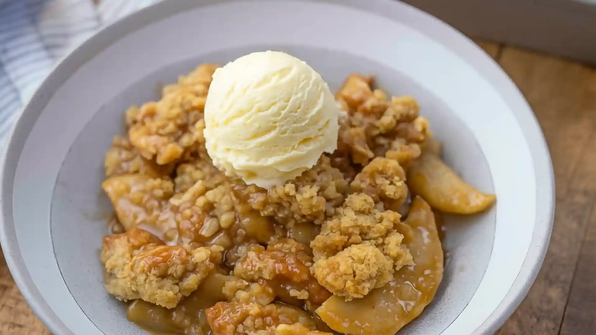 Bowl of warm apple crisp with cinnamon-spiced apples, topped with a scoop of vanilla ice cream.