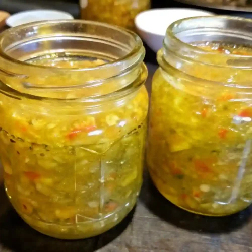 Close-up of two glass jars filled with homemade sweet pickle relish on a dark kitchen counter