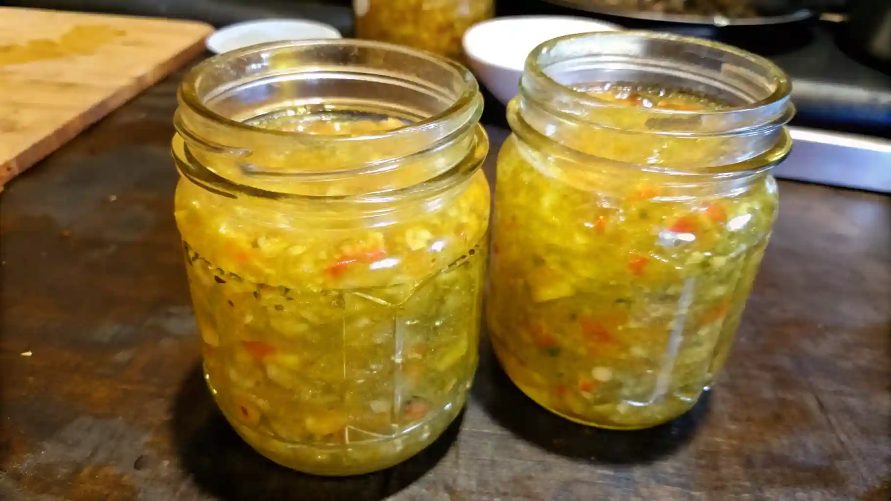 Close-up of two glass jars filled with homemade sweet pickle relish on a dark kitchen counter