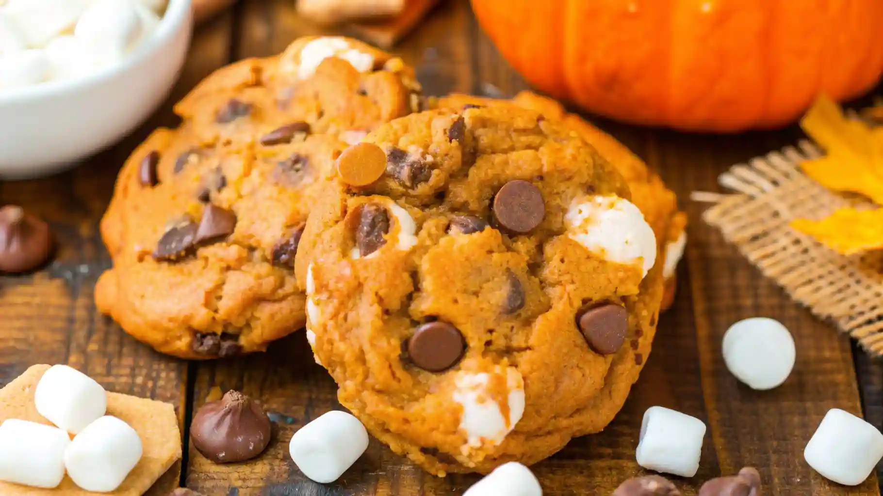Freshly baked Pumpkin S’mores Cookies with melted chocolate chips and marshmallows on a rustic wooden table