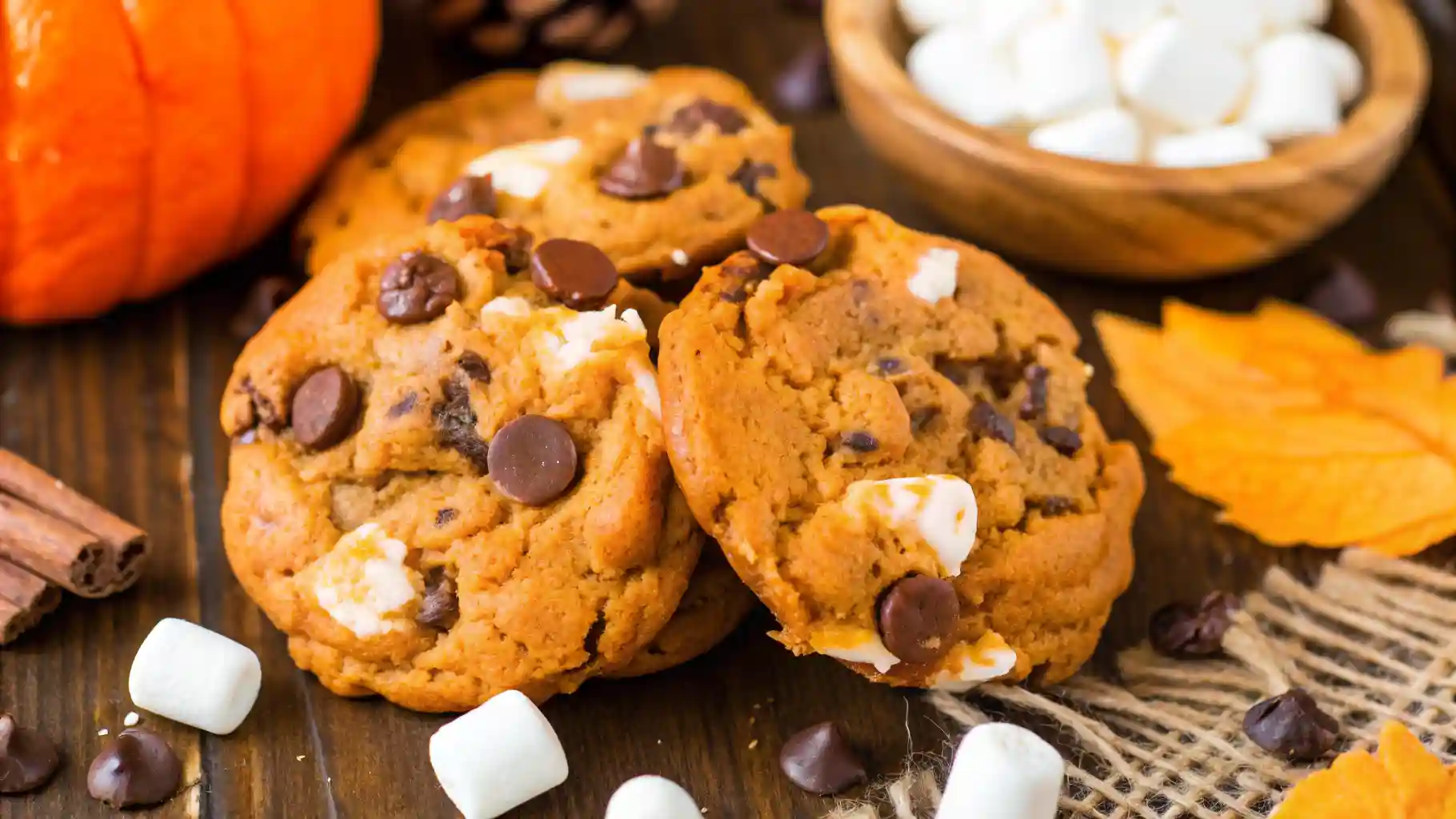 Pumpkin S’mores Cookies with chocolate chips and marshmallows styled with fall leaves and cinnamon sticks