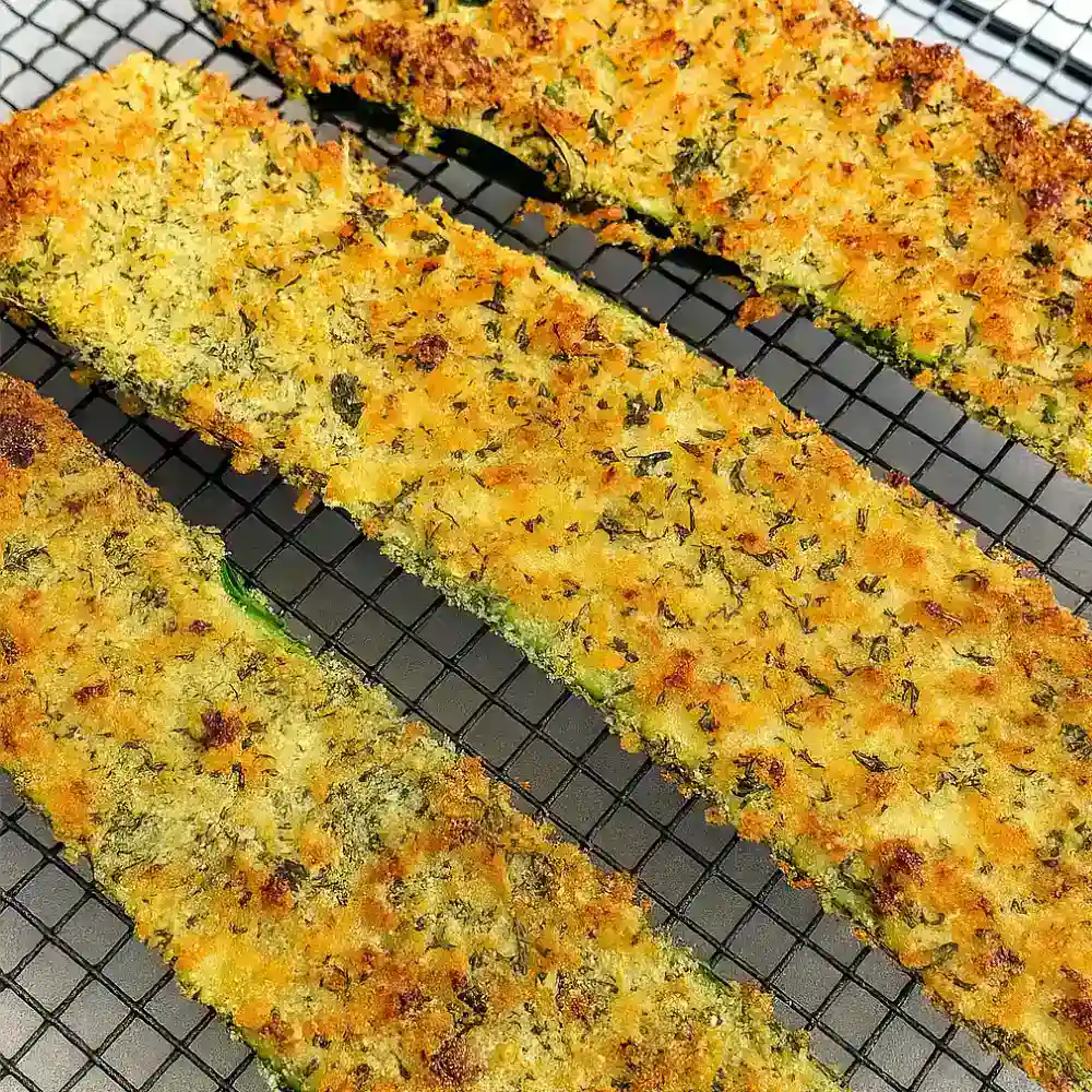 Golden baked zucchini slices with herbed panko crust on cooling rack for Three Cheese Zucchini Parmesan