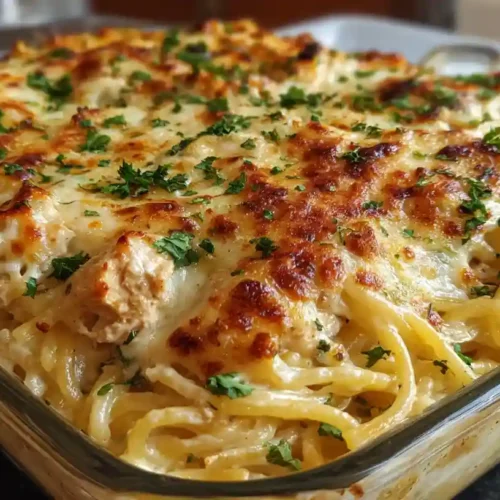 Golden cheesy chicken spaghetti casserole with creamy layers and crispy topping, garnished with fresh parsley in a glass baking dish.