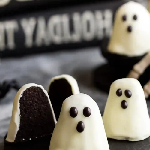 Ghost Oreo balls with white chocolate coating, one cut open to show the dark Oreo filling inside
