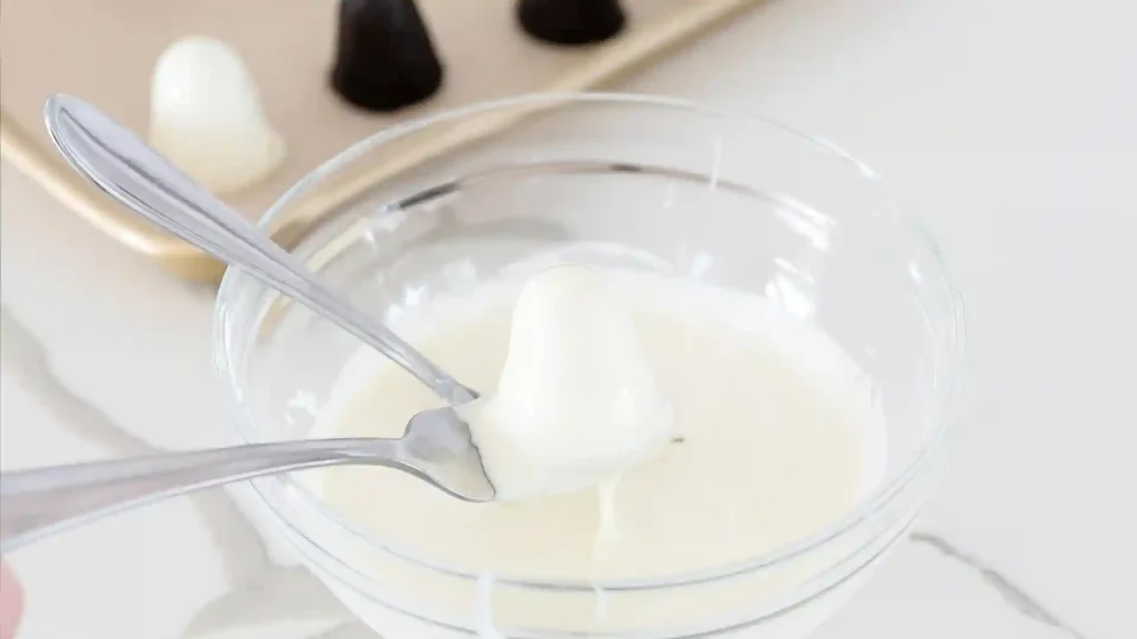 Shaped Oreo ball being dipped in melted white chocolate using forks during Halloween treat preparation