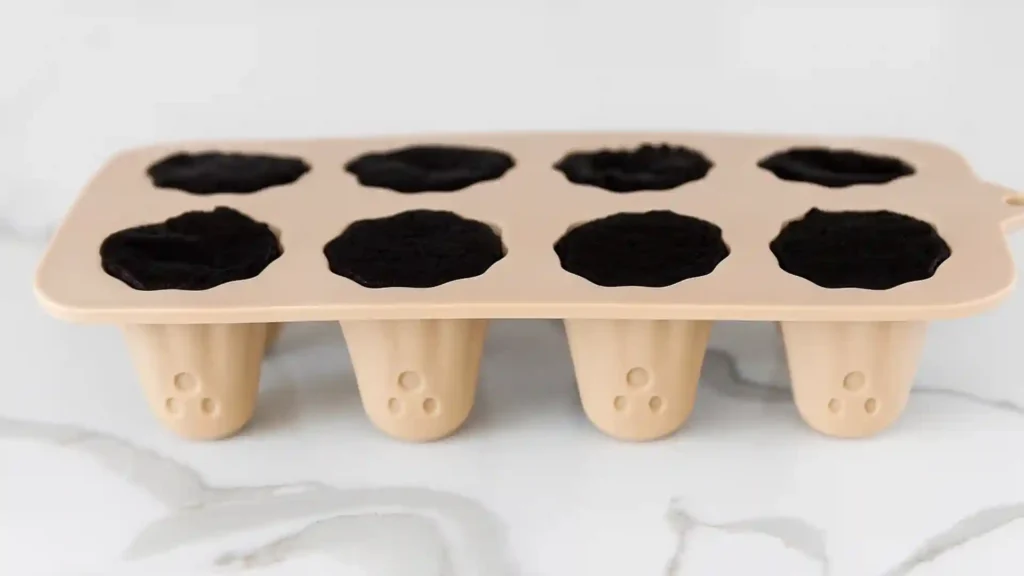 Ghost-shaped silicone mold filled with crushed Oreo and cream cheese mixture for Oreo balls